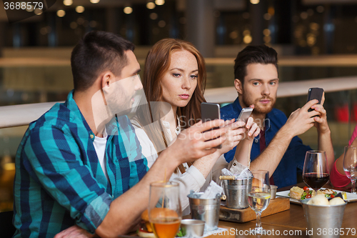 Image of friends with smartphones dining at restaurant