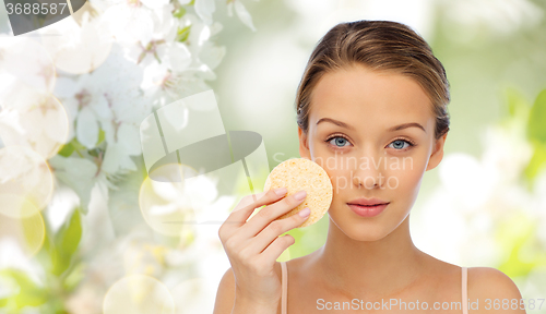 Image of young woman cleaning face with exfoliating sponge