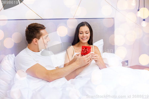 Image of happy man giving woman little red gift box in bed