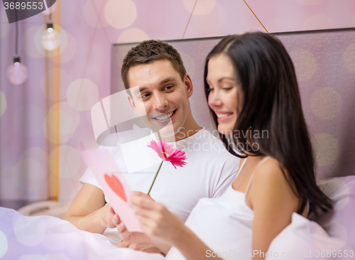 Image of smiling couple in bed with postcard and flower