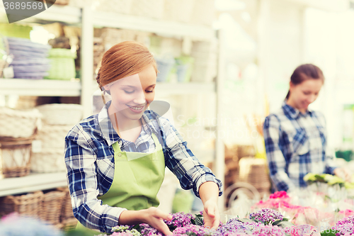 Image of happy woman taking care of flowers in greenhouse