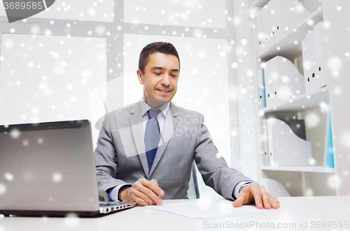 Image of smiling businessman with laptop and papers