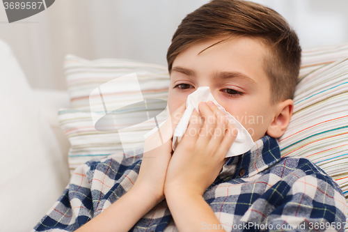 Image of ill boy lying in bed and blowing his nose at home