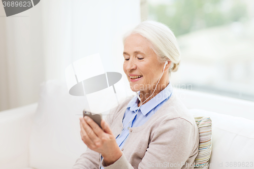 Image of senior woman with smartphone and earphones at home