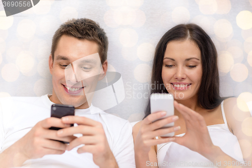 Image of smiling couple in bed with smartphones