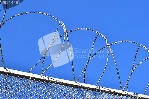 Image of Fence with a barbed wire against the blue sky. 