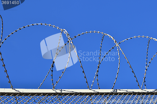 Image of Fence with a barbed wire against the blue sky. 