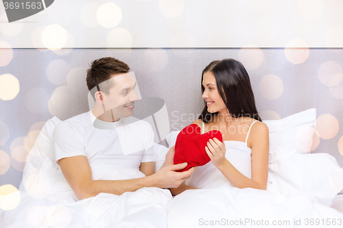 Image of smiling couple in bed with red heart shape pillow