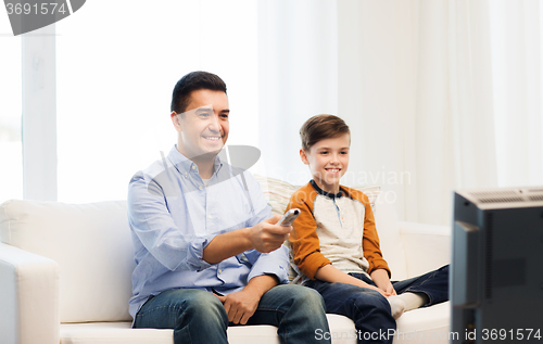 Image of smiling father and son watching tv at home