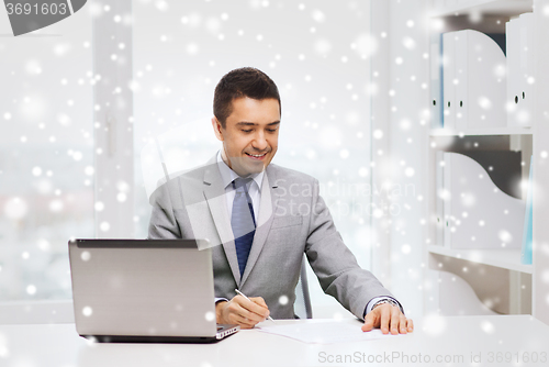 Image of smiling businessman with laptop and papers