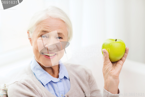 Image of happy senior woman with green apple at home