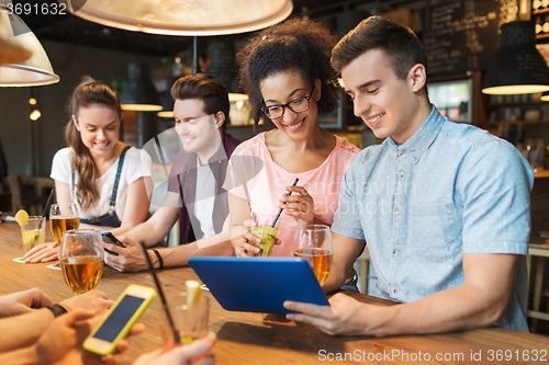 Image of happy friends with tablet pc and drinks at bar