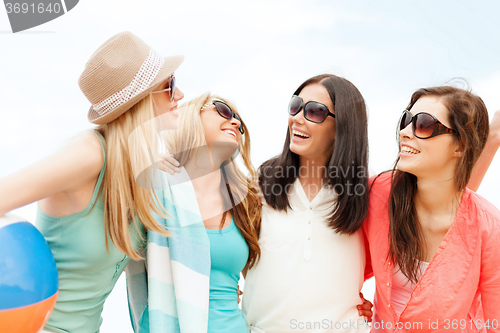 Image of smiling girls with ball and towel on the beach