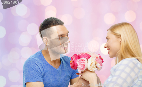 Image of smiling man giving woman flowers at home