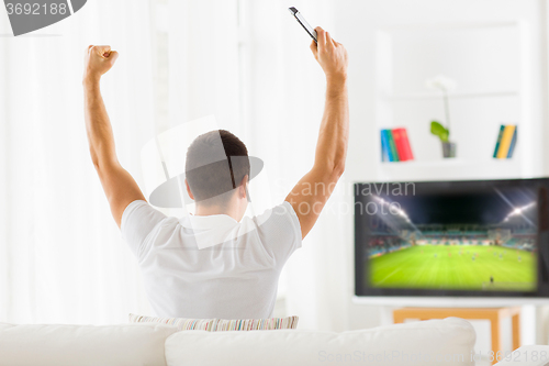 Image of happy man watching football on tv at home