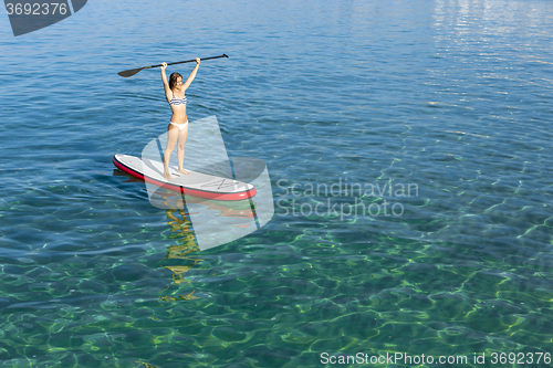 Image of A beautiful and happy woman with arms up and learning paddle-sur