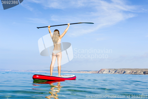 Image of A beautiful and happy woman with arms up and learning paddle-sur