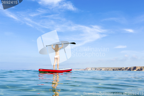 Image of A beautiful and happy woman with arms up and learning paddle-sur