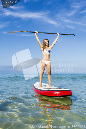 Image of A beautiful and happy woman with arms up and learning paddle-sur