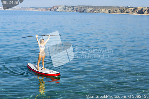 Image of A beautiful and happy woman with arms up and learning paddle-sur