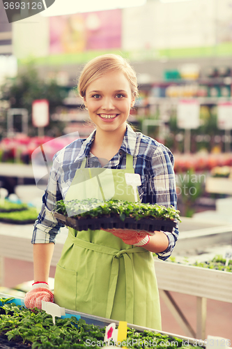 Image of happy woman holding seedling in greenhouse