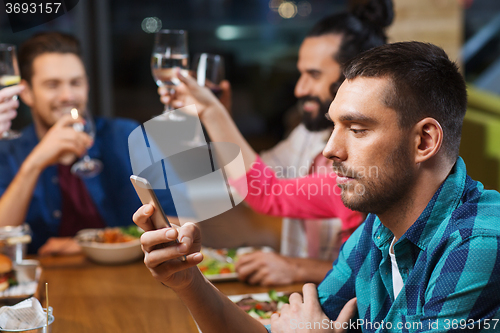 Image of man with smartphone and friends at restaurant