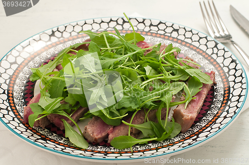 Image of Sliced beef cooked in the oven with salt, pepper and rocket