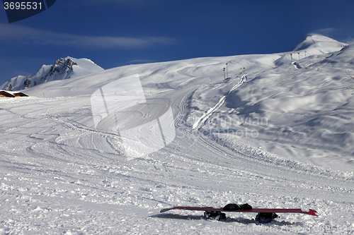 Image of Snowboard in snow on ski slope at sun windy evening