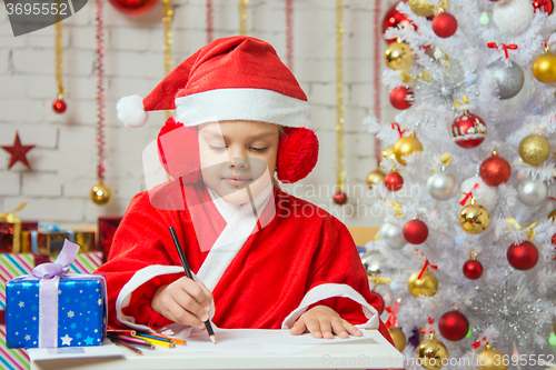 Image of Girl dressed as Santa Claus writing on a sheet of paper sitting at the table