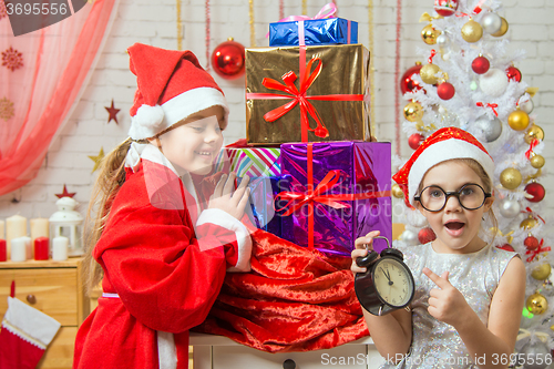 Image of Girl with surprise shows at the clock in the New Year, santa claus smiling happily unpacking gifts