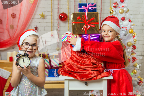 Image of One girl keeps watch over time, 11-55, another in a suit of Santa Claus hugging a bag with gifts