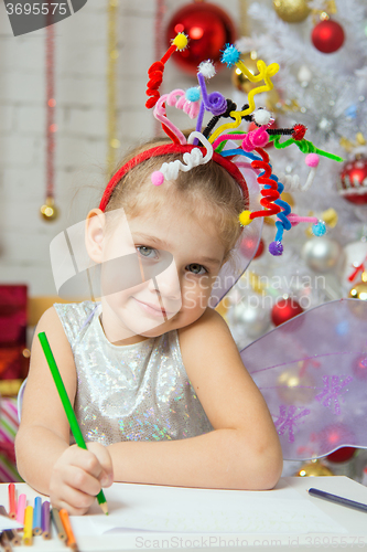 Image of Girl with a toy fireworks on the head draws pencil on a sheet