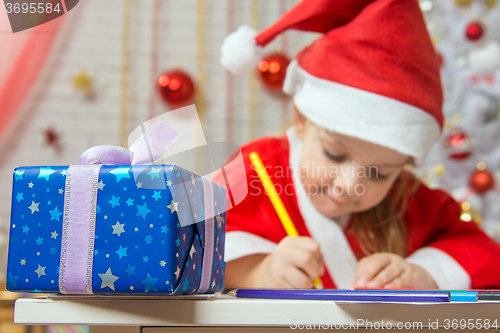 Image of New Years gift in the foreground, in the background Girl draws pencil