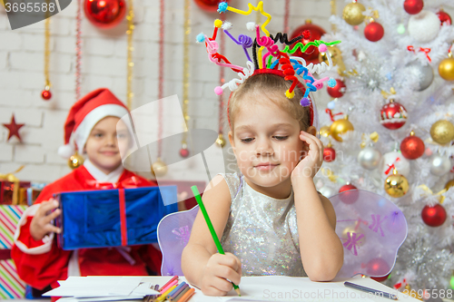 Image of She writes a letter to Santa Claus, who is sitting with a gift behind her