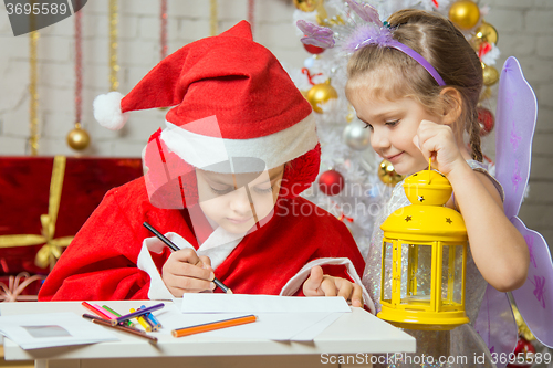 Image of Girl dressed as Santa Claus signs the envelope with a letter, standing next to the fairy girl with a flashlight in his hand
