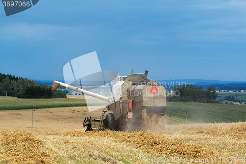 Image of old combine on field harvesting gold wheat