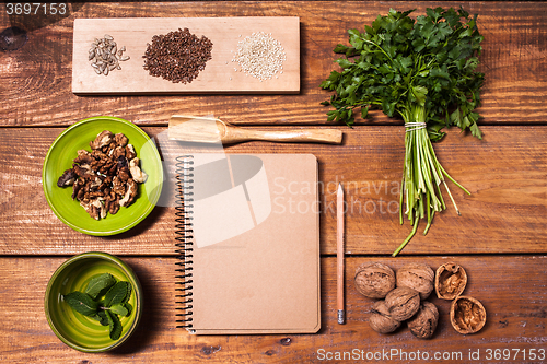 Image of Notebook for recipes, walnuts, parsley and seeds on wooden table.