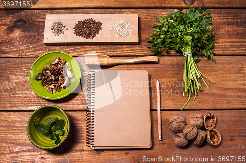 Image of Notebook for recipes, walnuts, parsley and seeds on wooden table.