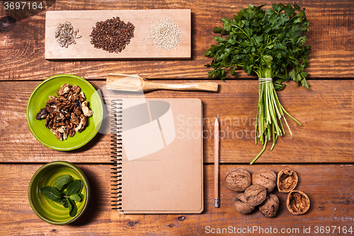 Image of Notebook for recipes, walnuts, parsley and seeds on wooden table.