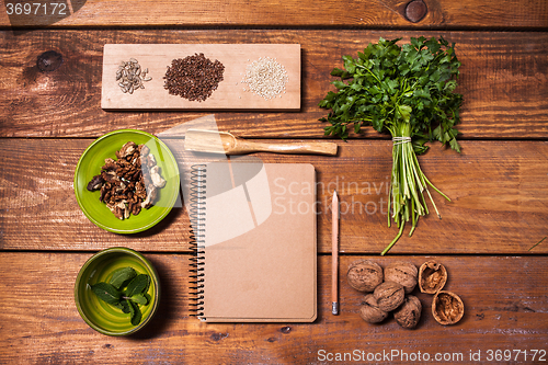 Image of Notebook for recipes, walnuts, parsley and seeds on wooden table.