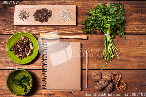 Image of Notebook for recipes, walnuts, parsley and seeds on wooden table.