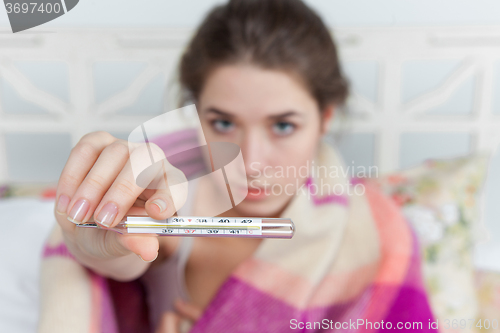 Image of Young sick woman in blanket with thermometer 