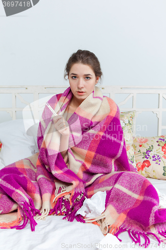 Image of Young sick woman in blanket with thermometer 