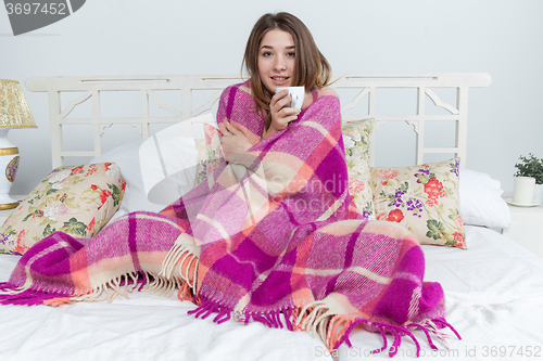 Image of Sick woman covered with blanket holding cup of tea