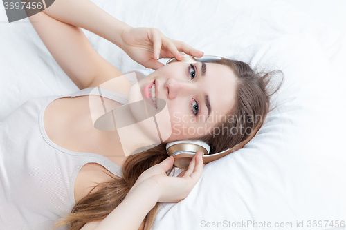 Image of The young girl in bed listening to music headphones