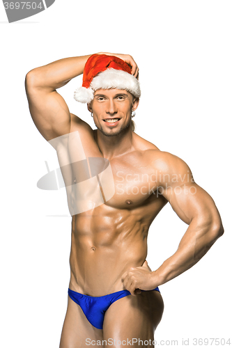 Image of Attractive young muscle man smiling in Santa Claus\'s red hat