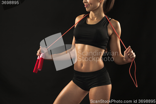 Image of Muscular young woman athlete with a skipping rope on black 