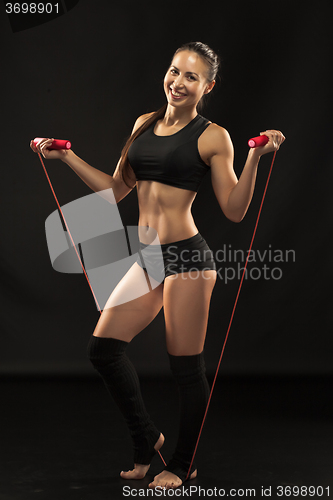 Image of Muscular young woman athlete with a skipping rope on black 