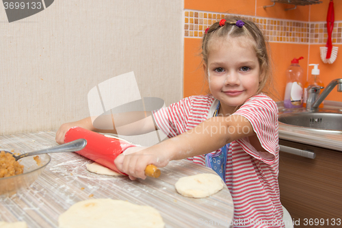 Image of The girl rolls the dough with a rolling pin pancake for pies and looks in the picture