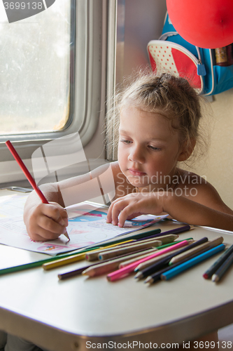 Image of Four-year girl drawing with pencils at a table in a train